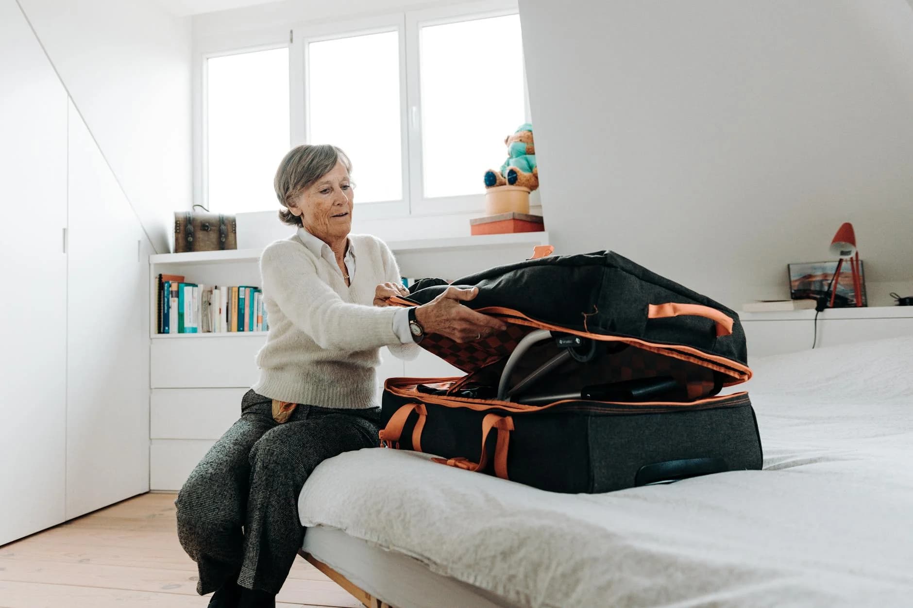 Elderly Woman Sits On Bed Packing A Suit 2