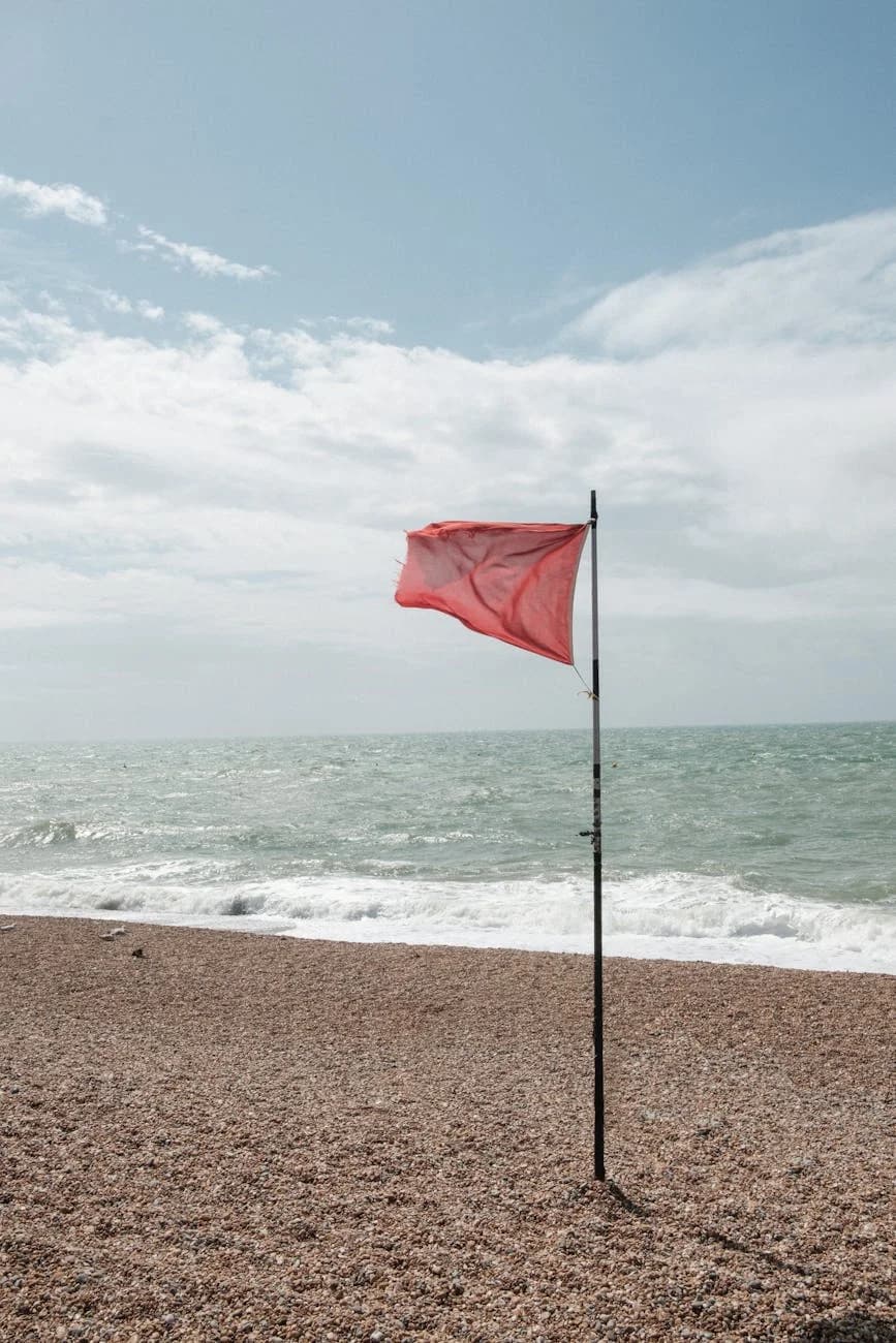 A Striking Red Flag Flutters On A Pebble 3