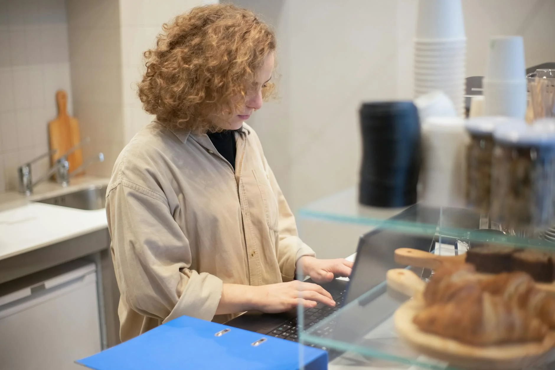 Una joven usa una laptop detrás de un mostrador de café
