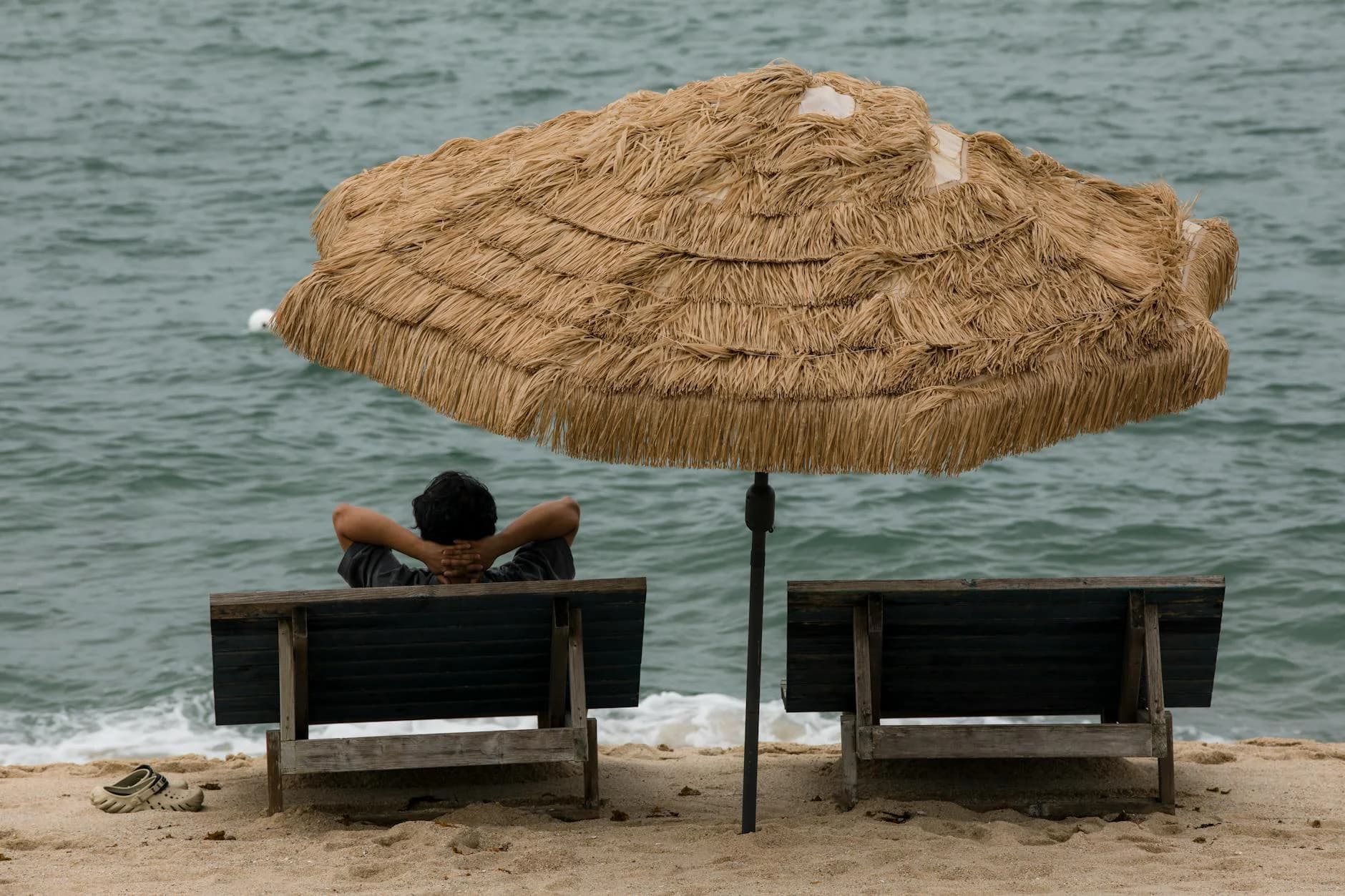 A Person Relaxes On A Beach Under A Stra 1